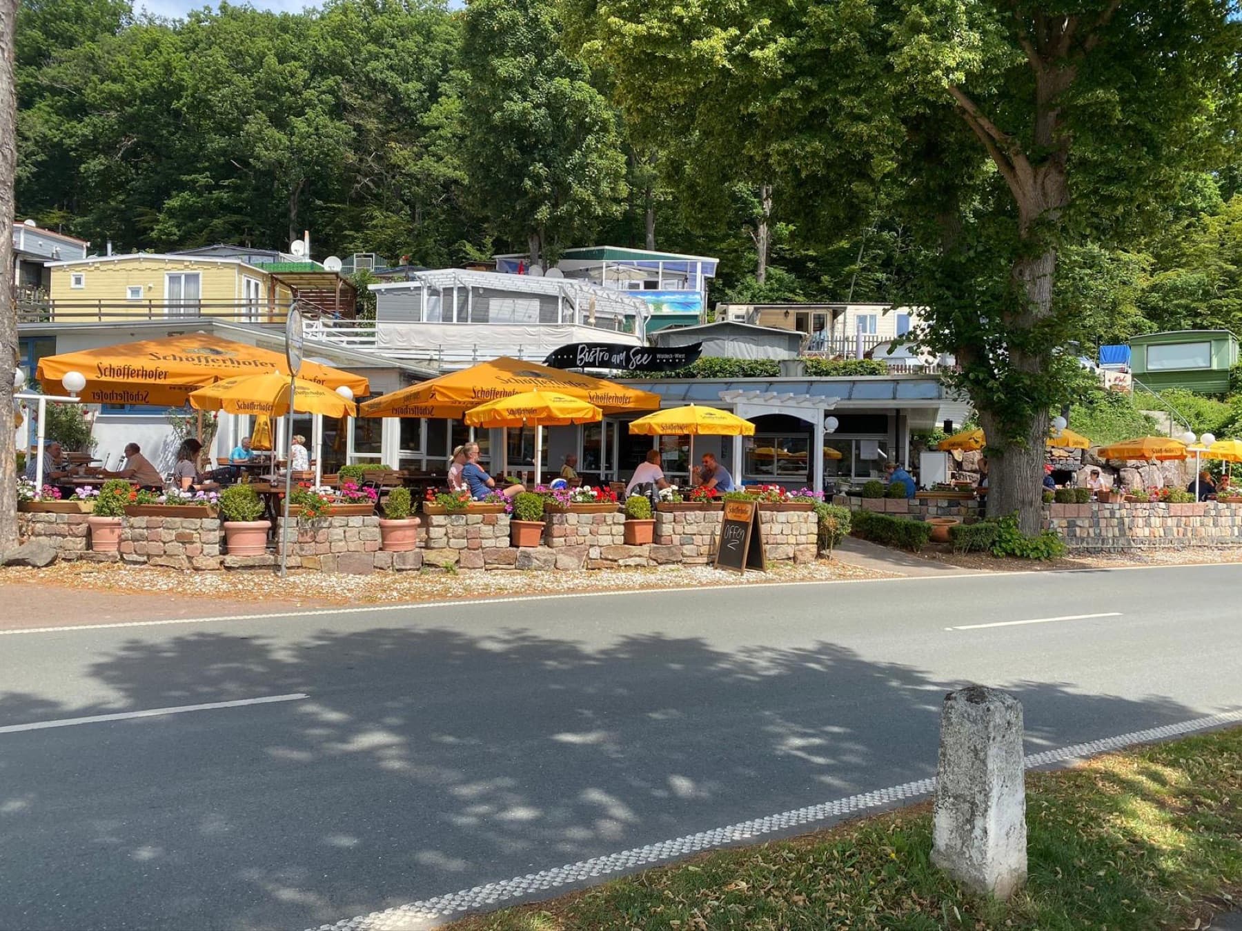 Das Bistro am See mit orangen Sonnenschirmen an der Uferstraße
